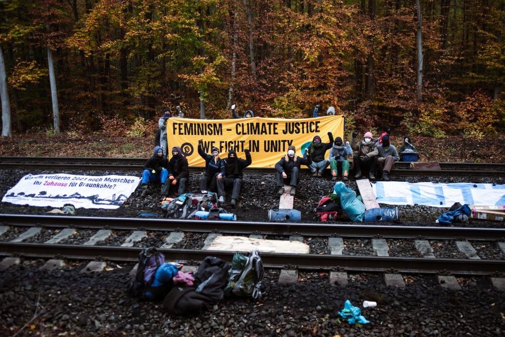 Menschen auf Schienen mit Transparent "Feminism - climate justice - we fight in unity"