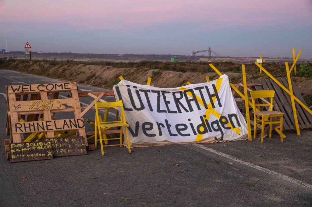 Barrikade "Welcome to ZAD Rhineland" mit Stühlen und Braunkohlebagger im Hintergrund