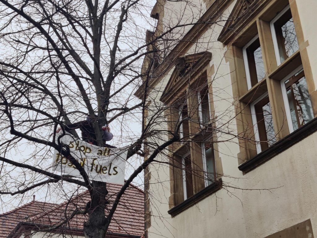Person im Baum vorm Gerichtsgebäude mit Transparent "Stop all fossil fuels"