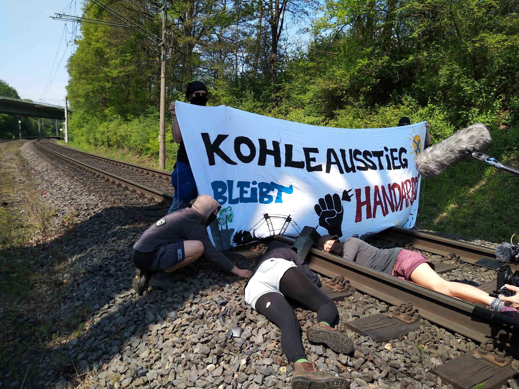 Menschen auf Gleisen mit Transparent "Kohleausstieg bleibt Handarbeit" - Lock-On verkehrt herum auf dem Gleis
