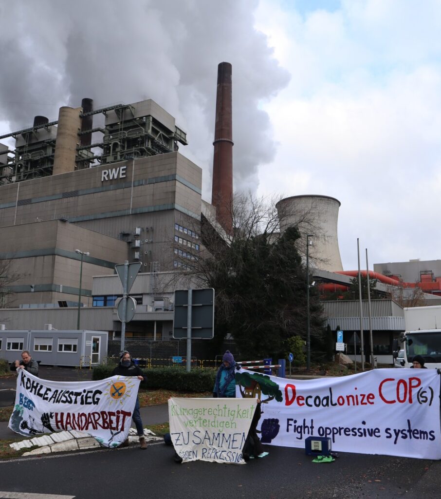 Blockade vorm Kohlekraftwerk Neurath, drei Transparente, Kraftwerk mit RWE-Logo im Hintergrund