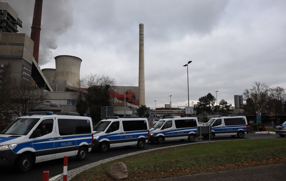 4 große Polizeiwannen hintereinander, im Hintegrund Kohlekraftwerk und klein Menschen von Blockade