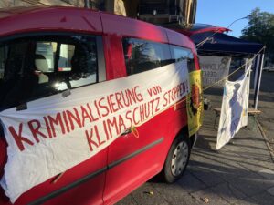 Auto mit angebrachtem Transparent "Kriminalisierung von Klimaschutz stoppen", im Hintergrund weitere Transparente.