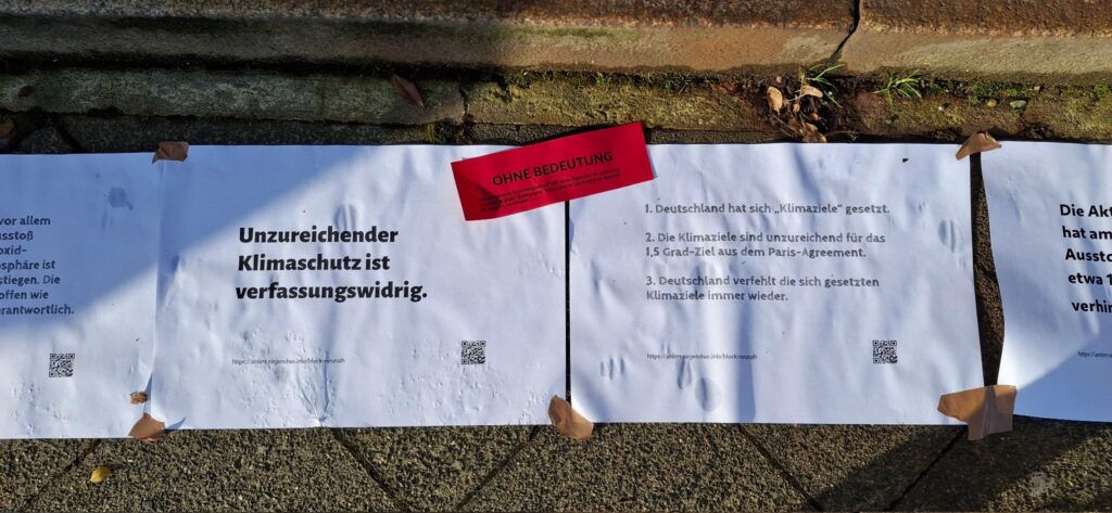 Zwei Plakate kleben auf dem Boten, auf einem die Aufschrift "Unzureichender Klimaschutz ist verfassungswidrig", auf einem roten Aufkleber darüber die Botschaft "Ohne Bedeutung"