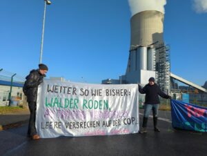 Zwei Menschen halten vorm Kohlekraftwerk im Sonnenschein ein Transparent "weiter so bisher: Wälder roden - Aktivistis verurteilen - leere Versprechen auf der COPS - #FuckRWE #SündiBleibt"